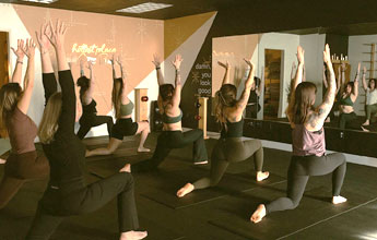 Group of women holding arms overhead in a low lunge during a yoga class at Bloom studio in Coos Bay.