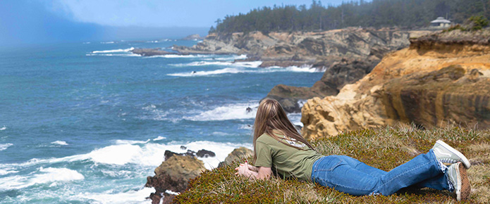 young woman laying on ground near cliff overlooking pacific ocean