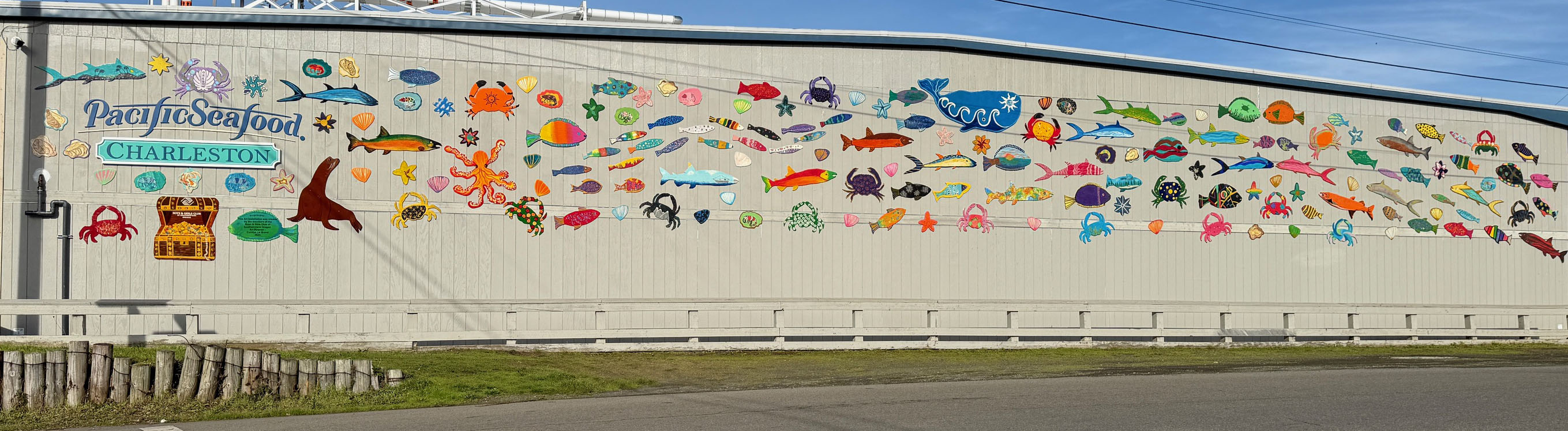 The Boys & Girls Club created this colorful mural of fish and mammels! A mural of colorful fish adorn the outside of a warehouse building.