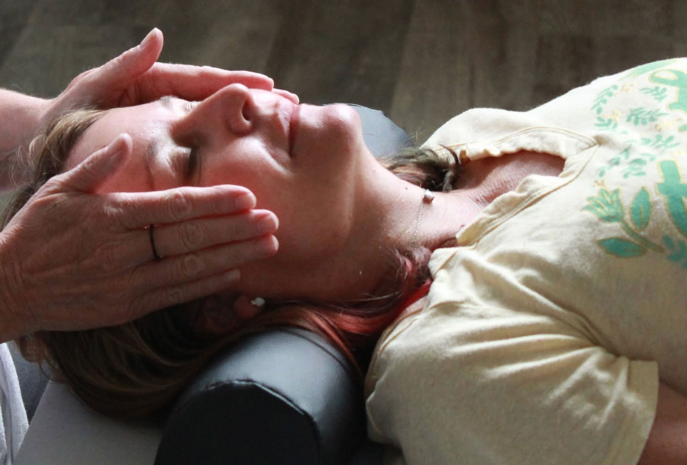 A practitioner administers a Reiki energy healing session with hands gently placed on a woman’s head as she rests with eyes closed.
