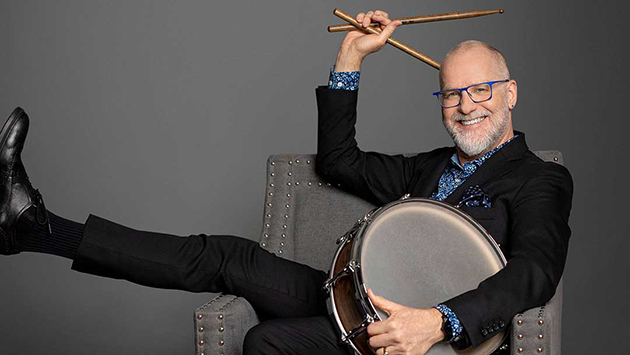Percussionist Terry Longshore joins the OCMA Orchestra II. Percussionist Terry Longshore sitting in a grey chair holding a drum and drum sticks.